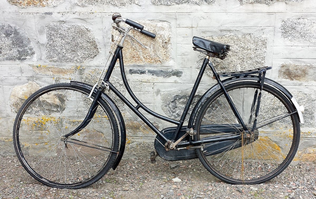 石の壁の前にとめられた、古い黒い自転車を横から見たところ