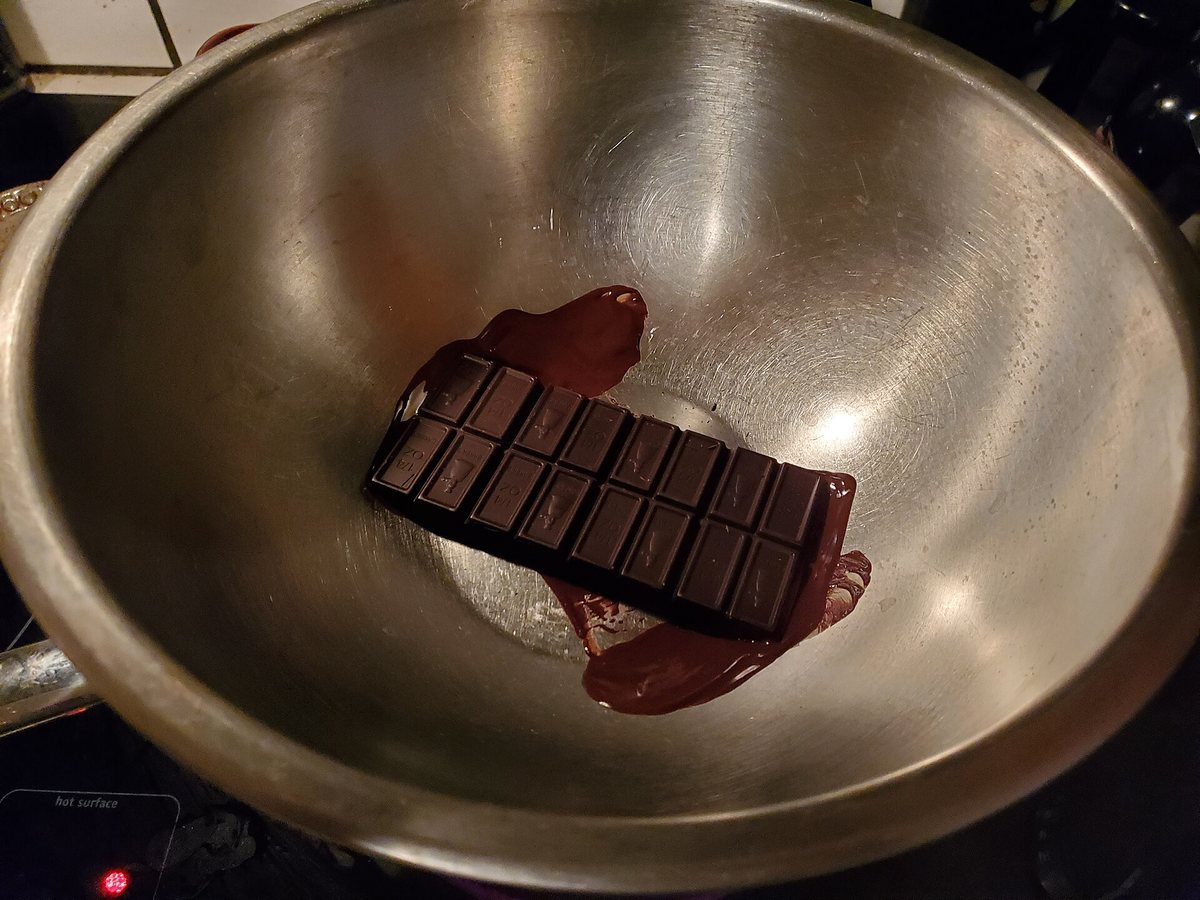 A chocolate bar in a bowl over warm water, starting to melt smoothly at the bottom