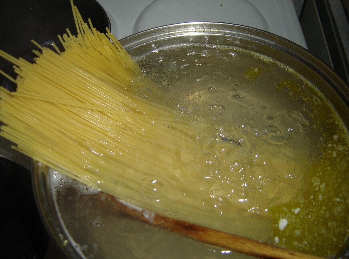Dry spaghetti in a pot of bubbling water, starting to bend where it is underwater